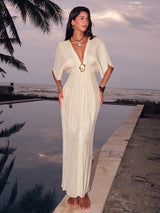Woman in a white dress standing by a pool with palm trees and ocean in the background