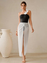 Woman wearing a black top and white skirt with a flower in her hair, standing next to a large white vase.