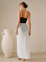Woman in a black top and white skirt standing next to a large white vase against a beige wall.
