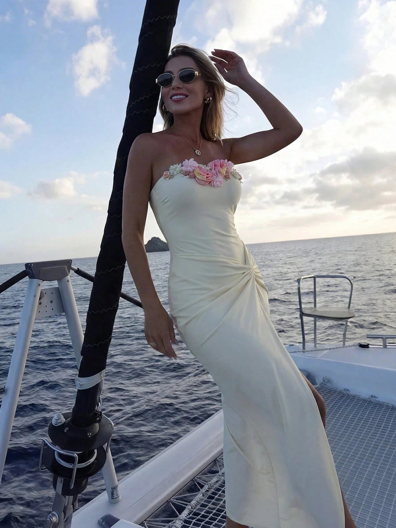 Woman in a strapless white dress with floral details on a boat with ocean and sky background