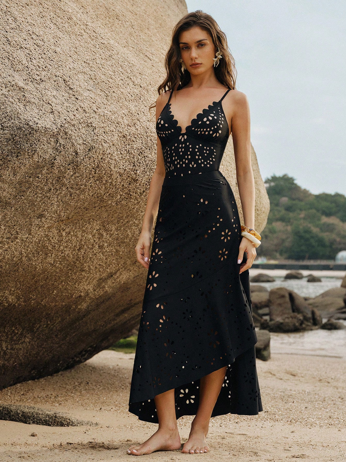 Woman in a black dress with cut-out details standing on a beach.