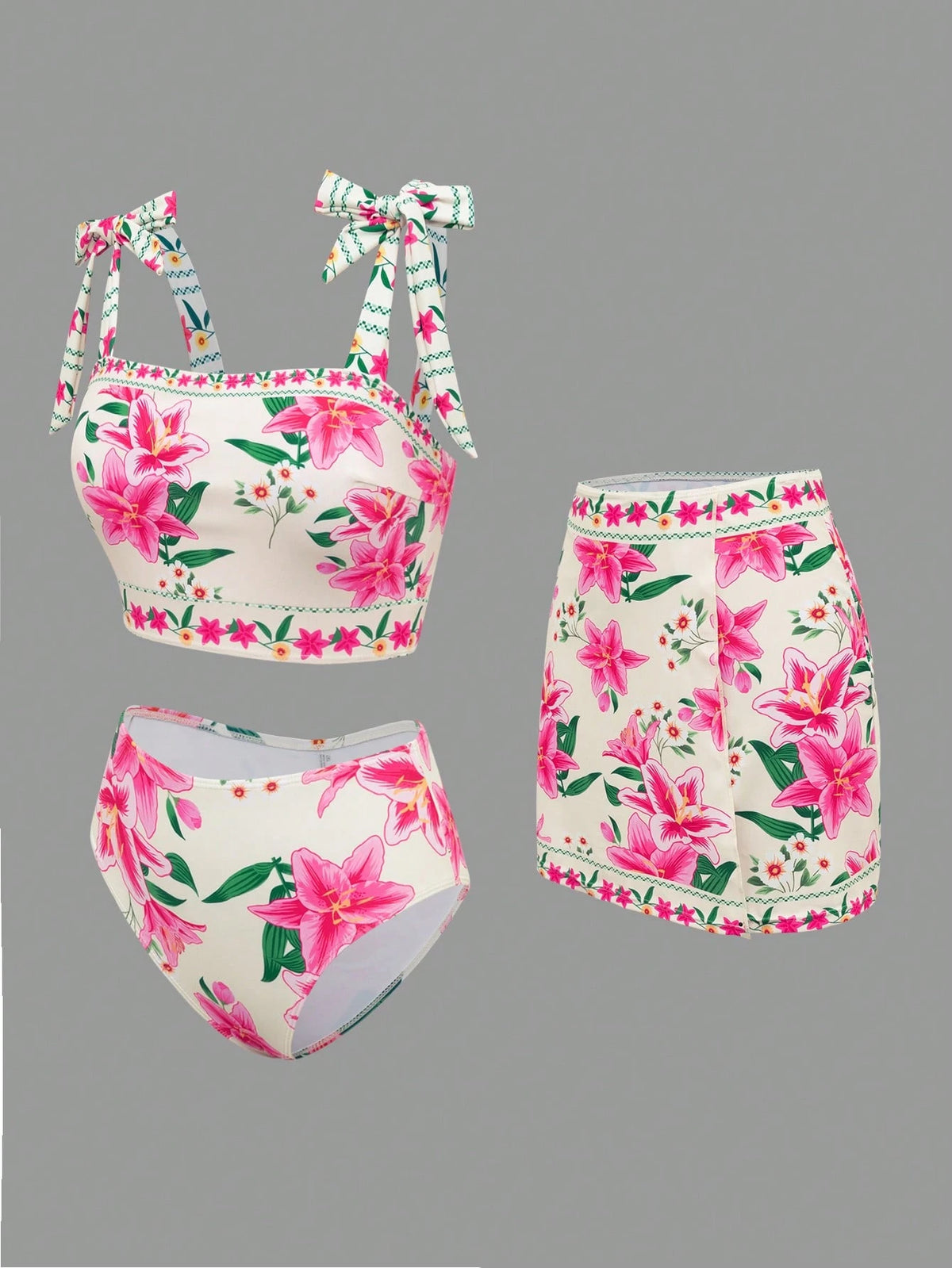 A three-piece bikini set featuring a pink and green floral print on a white base, including a tie-strap crop top, high-waisted mini skirt, and high-waisted bottoms, displayed against a solid gray background.