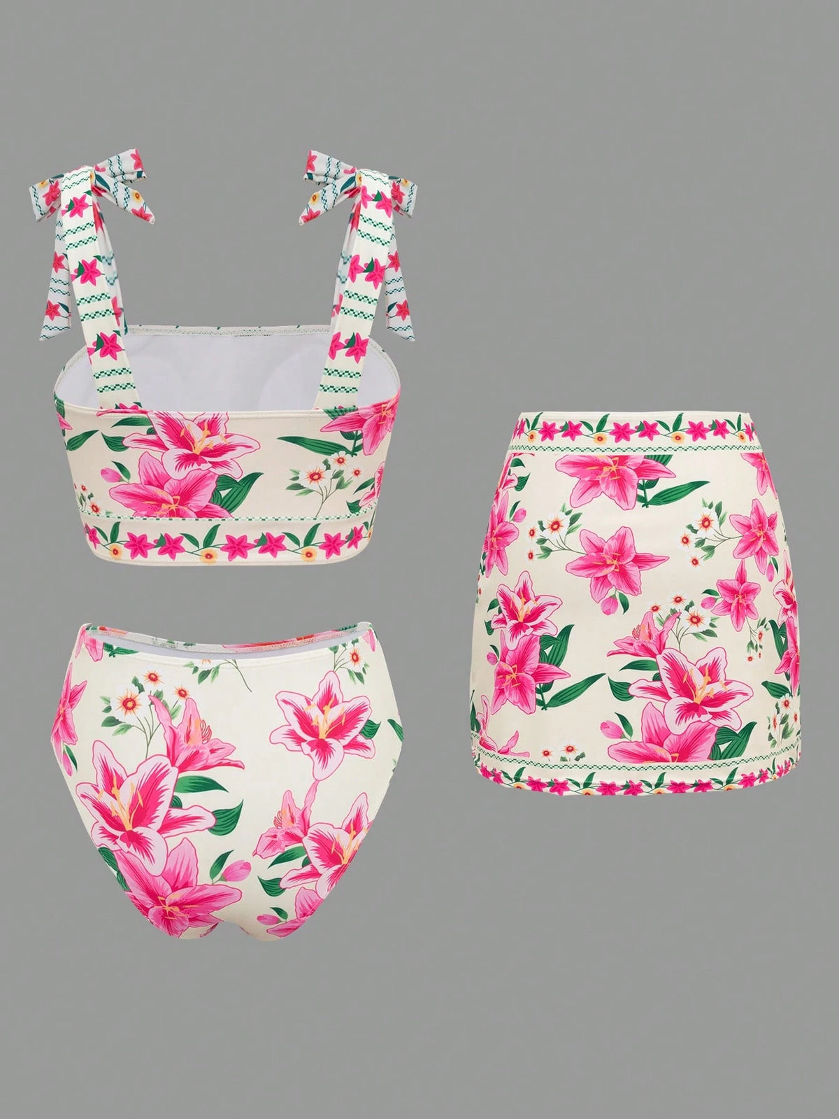 A three-piece girls' bikini set with a pink and green floral print on a cream background, featuring a tie-strap top, high-waisted bottoms, and a mini skirt, shown against a solid gray background.
