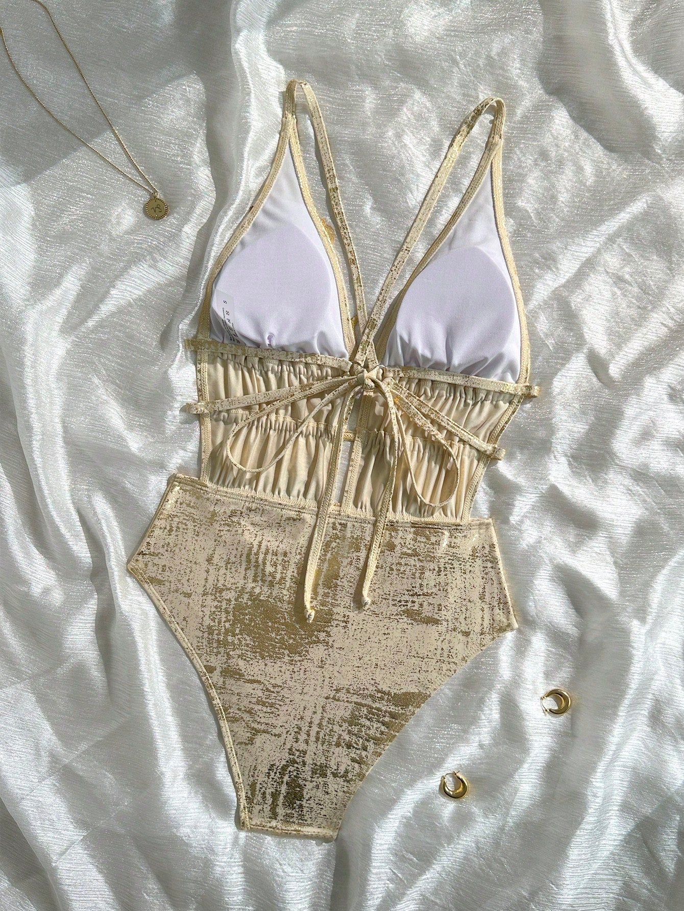 Beige and white swimsuit on a textured white surface with jewelry.
