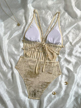 Beige and white swimsuit on a textured white surface with jewelry.