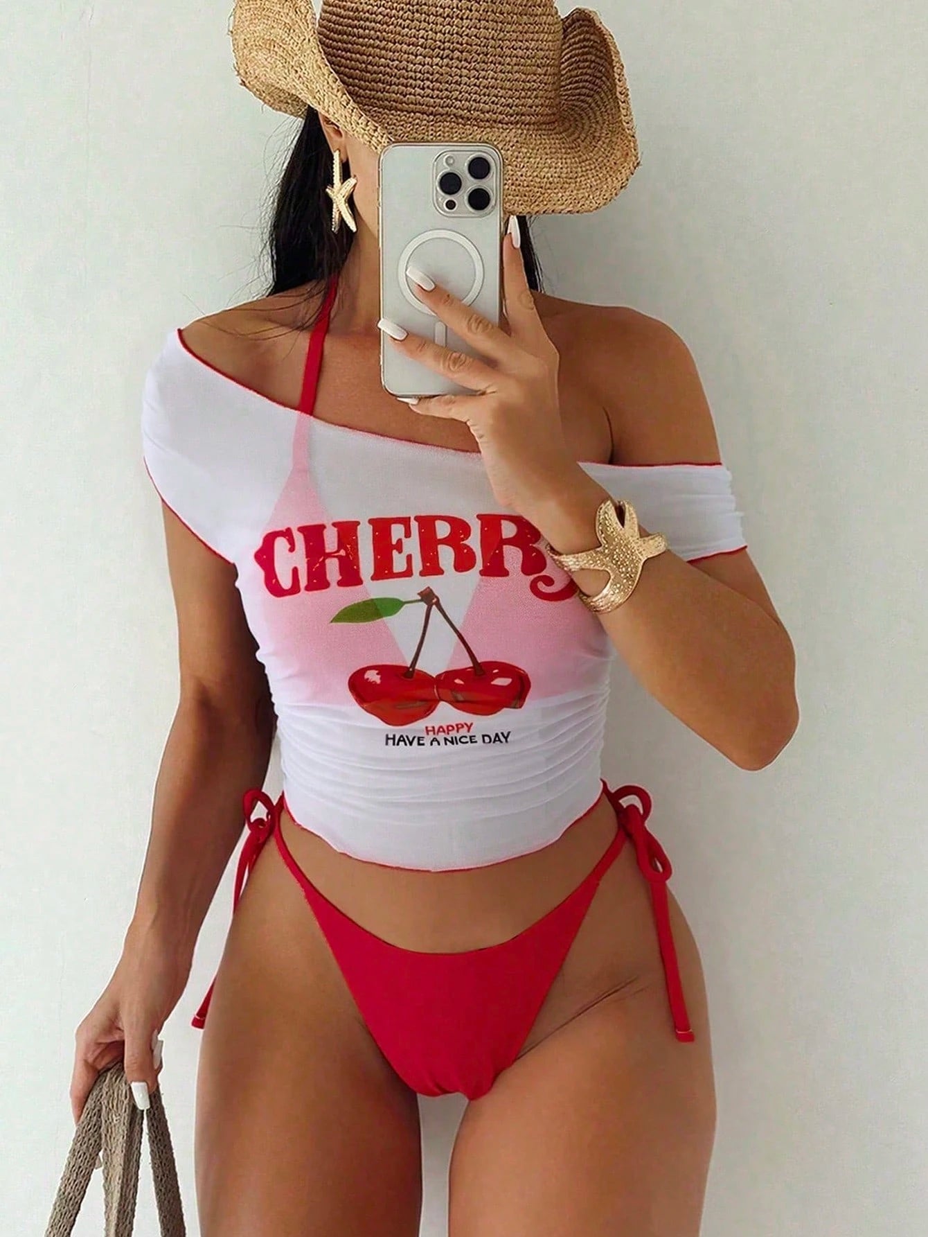 Person wearing a cherry-themed bikini with a white top and red bottoms, taking a mirror selfie.