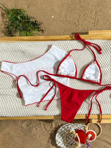 Red and white bikini set on a textured surface with sand and plants in the background