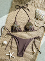 Brown bikini set with embellishments on a textured surface with shells and starfish.