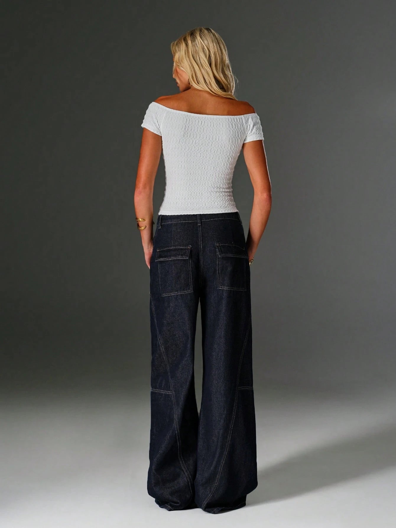 Woman wearing a white top and dark blue jeans against a gray background