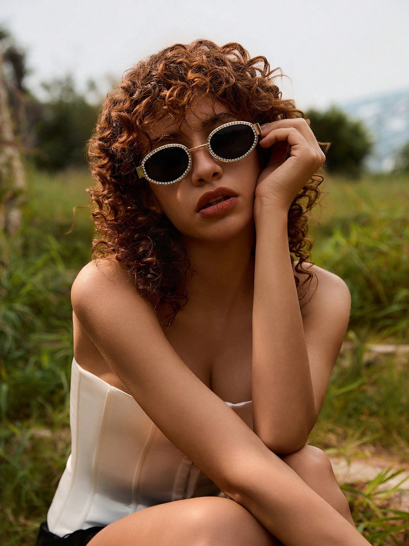Woman with curly hair wearing sunglasses in a natural setting