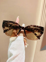 Leopard print sunglasses held by a hand against a neutral background