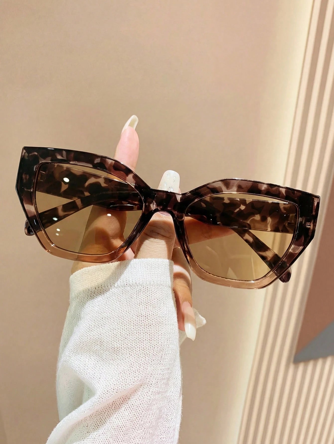 Leopard print sunglasses held by a hand against a neutral background