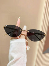 Sunglasses with gold frames and dark lenses held by a hand against a beige background
