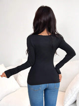 A woman with long dark hair is shown from behind wearing a fitted black long-sleeve top and blue jeans, standing in front of a white couch.