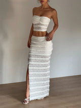 Woman wearing a strapless top and long skirt with a high slit, standing against a plain background.