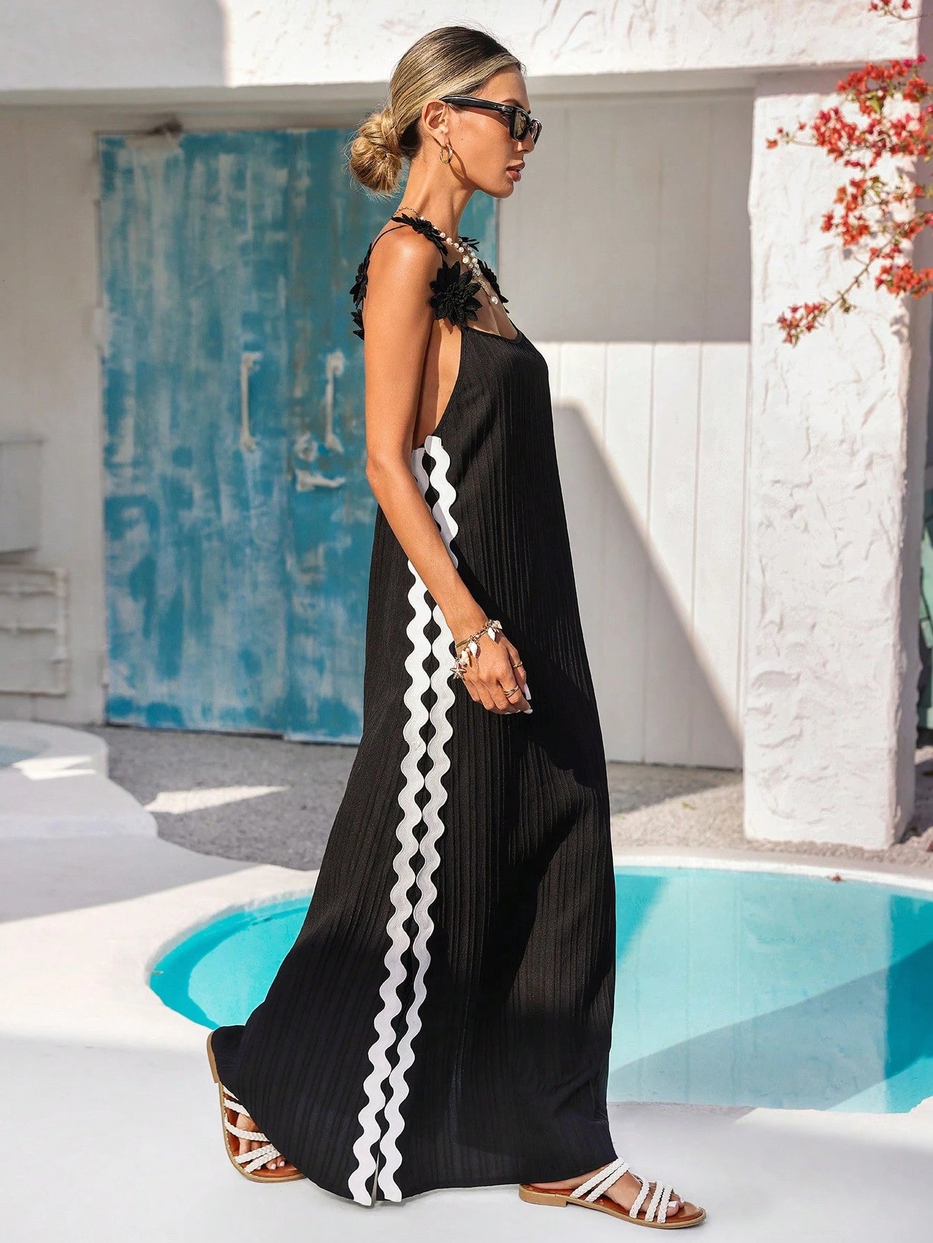 Woman wearing a black dress with white patterns by a poolside.