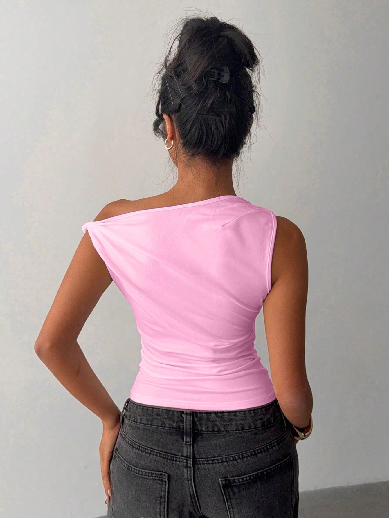 Person wearing a pink sleeveless top and dark pants against a plain background