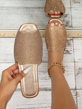 Gold embellished slippers worn by a person on a wooden floor.