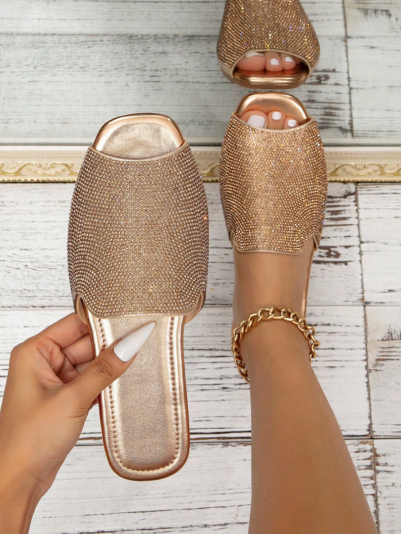 Gold embellished slippers worn by a person on a wooden floor.