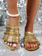 Gold sandals with fringe details worn by a person against a sparkling background