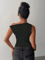 Person wearing a black one-shoulder top and gray pants against a plain background
