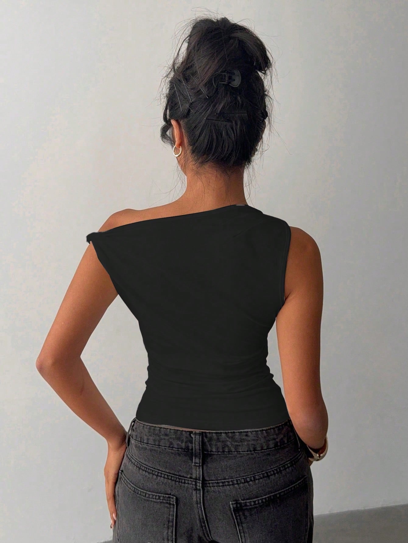 Person wearing a black one-shoulder top and gray pants against a plain background