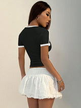 Woman wearing a navy blue top with white trim and a white skirt on a plain background