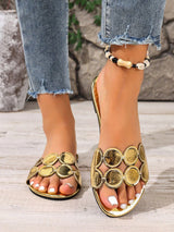 Gold sandals with circular designs worn by a person with ripped jeans.