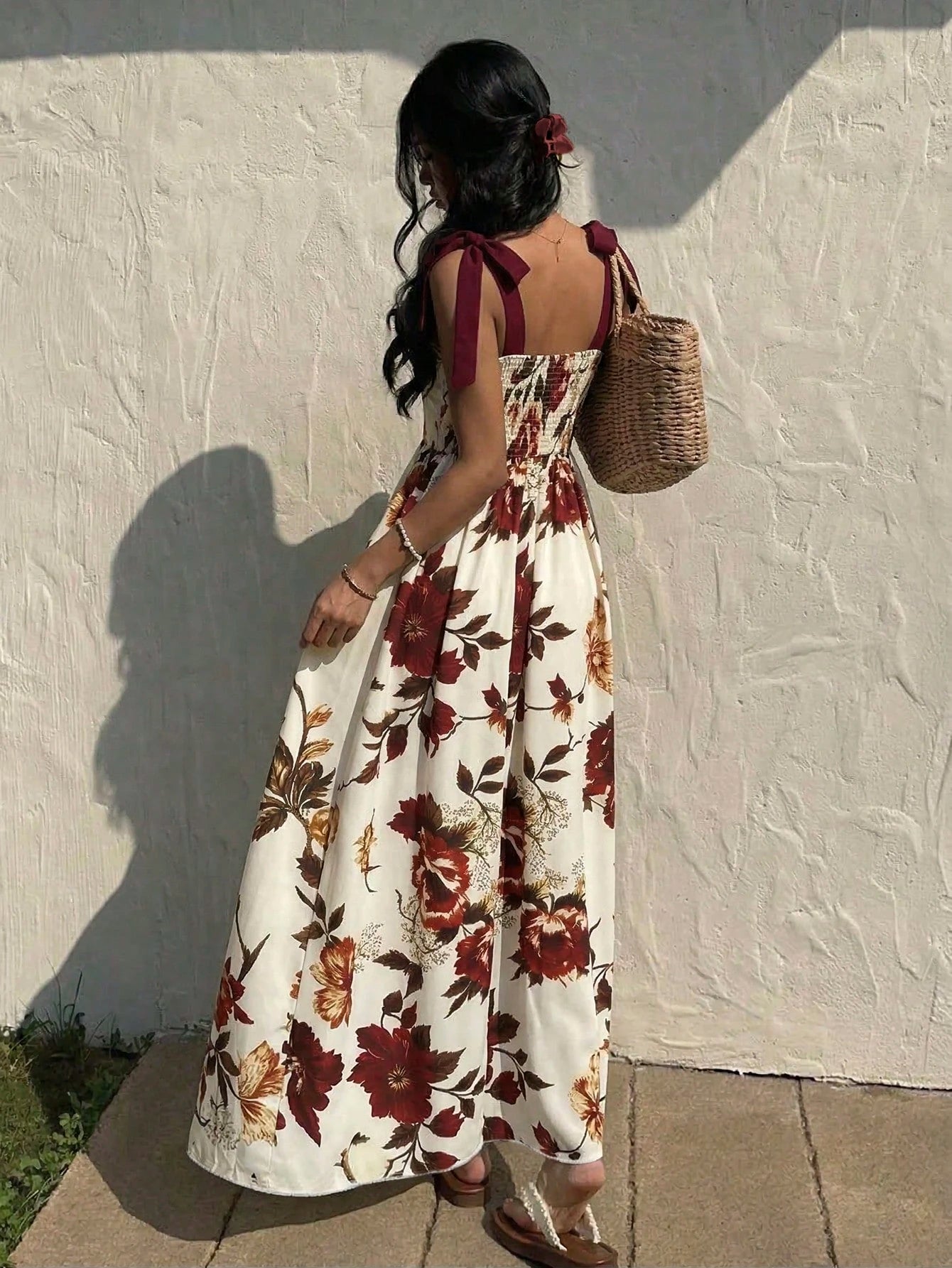 Woman in a floral dress standing against a textured wall.