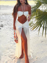 Woman in a white bikini and cover-up on a beach with palm leaves.