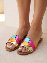 Colorful sandals with a rainbow strap pattern worn by a person on a neutral background