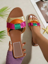 Brown sandal with colorful straps worn by a person, with a blurred indoor background.
