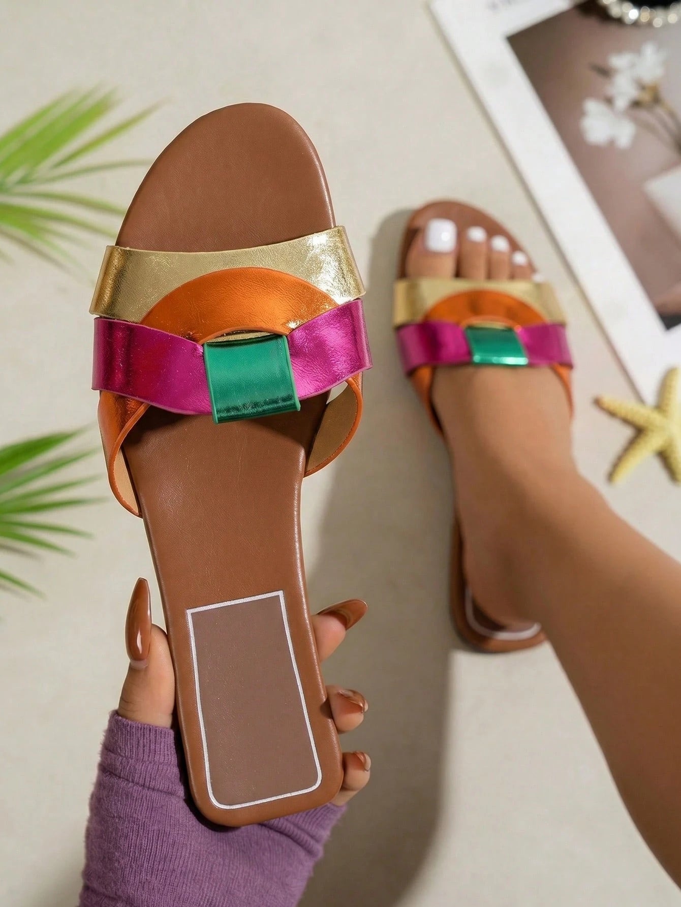 Brown sandal with colorful straps worn by a person, with a blurred indoor background.