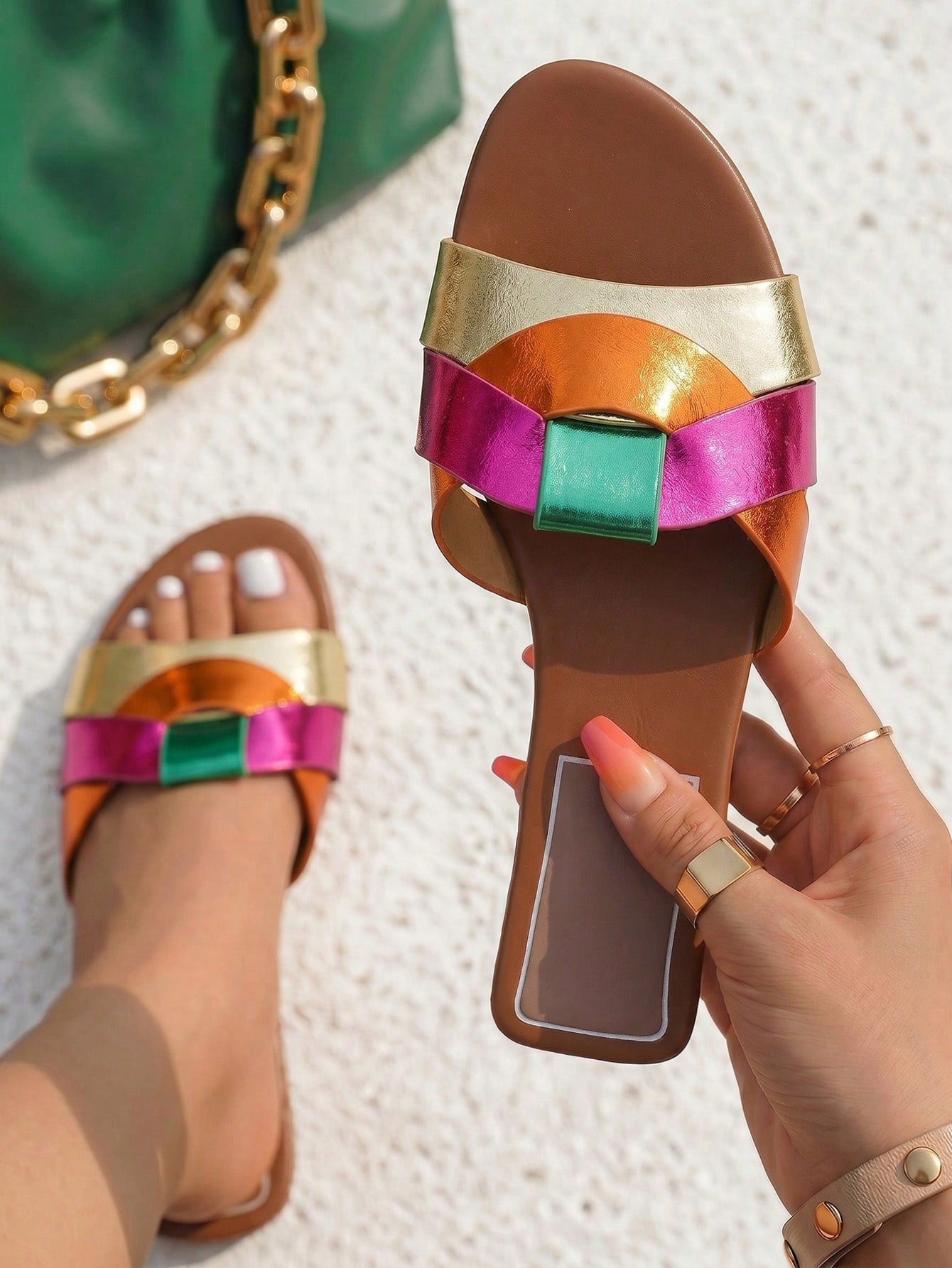 Colorful sandal with metallic straps held by a hand on a textured surface.
