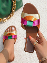 Colorful sandal with metallic straps held by a hand on a textured surface.