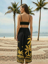Woman in black and yellow outfit standing on a beach with palm trees in the background