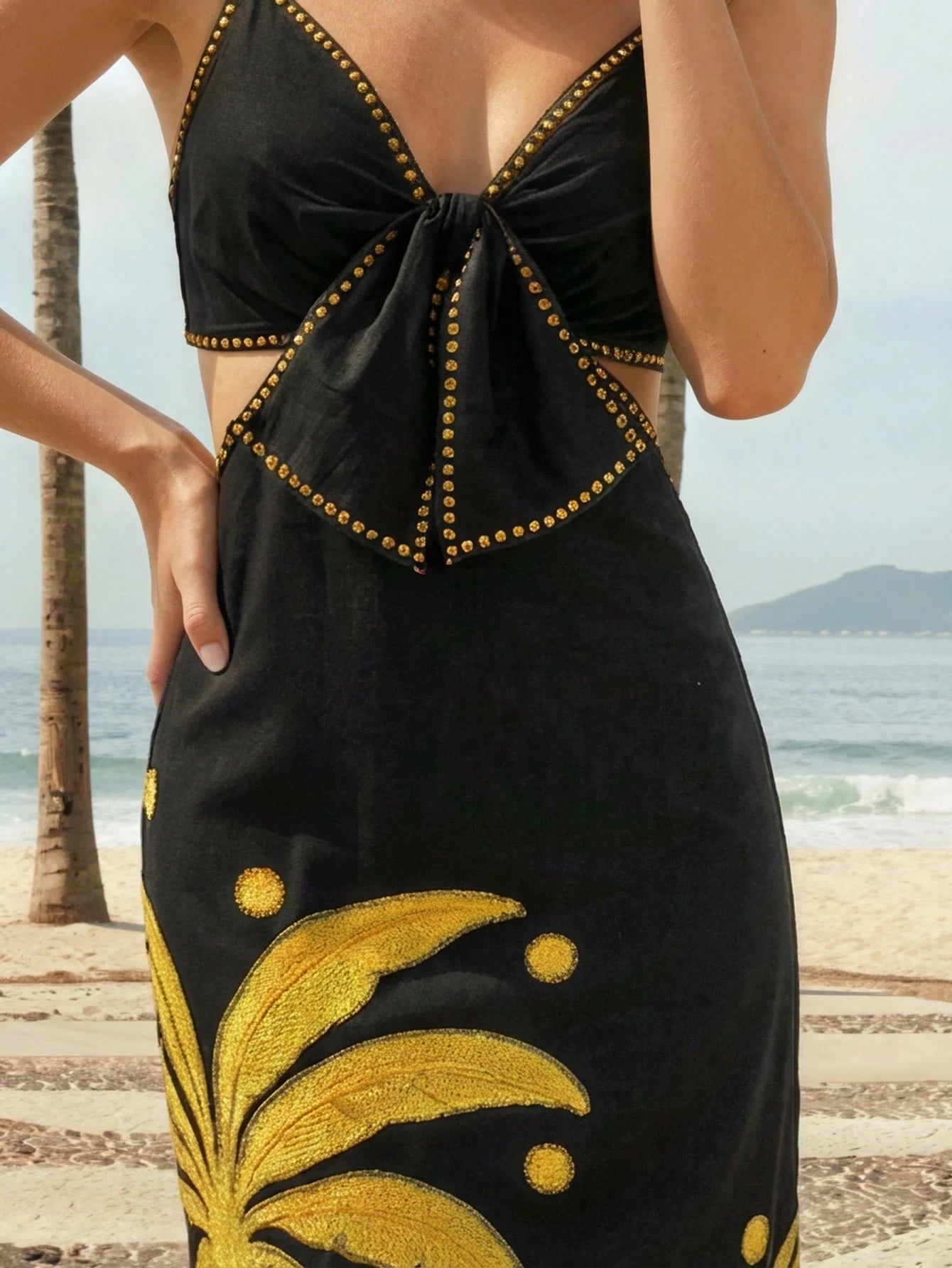Black dress with gold detailing and floral patterns on a beach